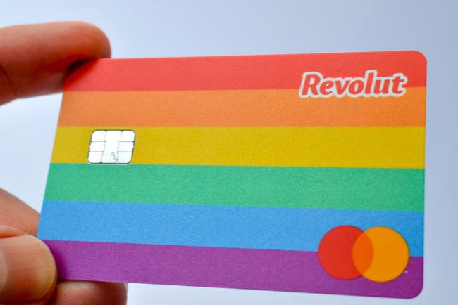 Tumme och pekfinger som håller i det nya regnbågsfärgade kreditkortet Revolut