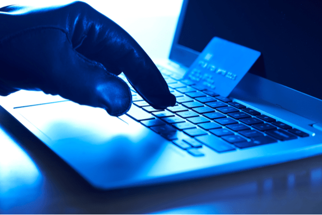 Cyberbrottslings hand med handske, bärbar dator och ett stulet kreditkort