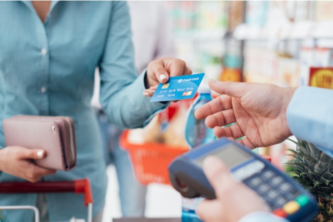 Kvinna sträcker fram betalkort till kassör i butik
