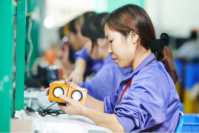 Kinesisk kvinna sitter och arbetar i en fabrik med linjeproduktion