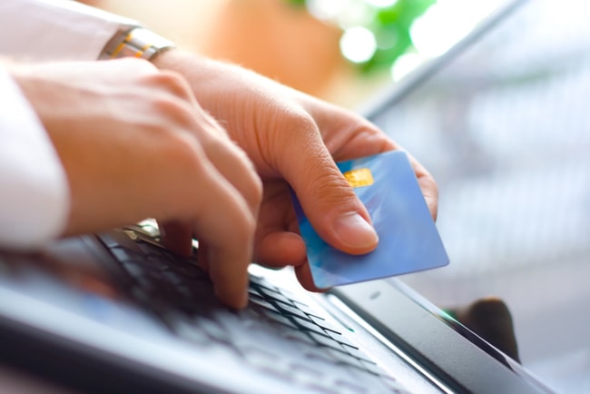 Ung man håller i ett betalkort och gör köp online.