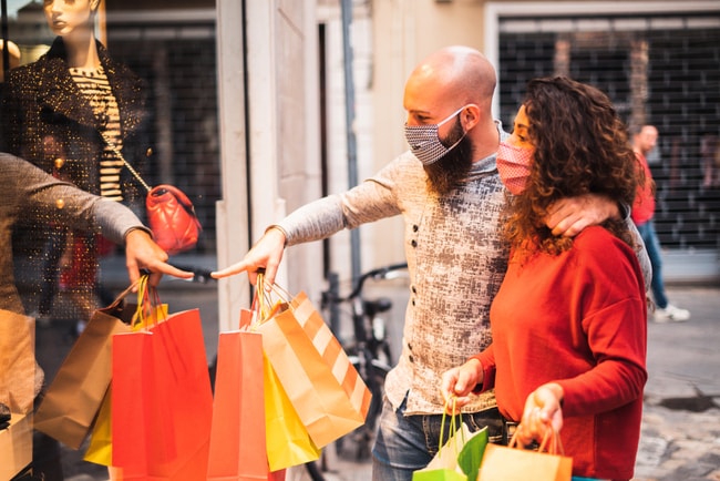 par med munskydd och shoppingkassar tittar i skyltfönster