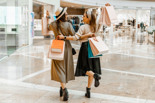 Två unga kvinnor i ett shoppingcentrum med shoppingkassar.